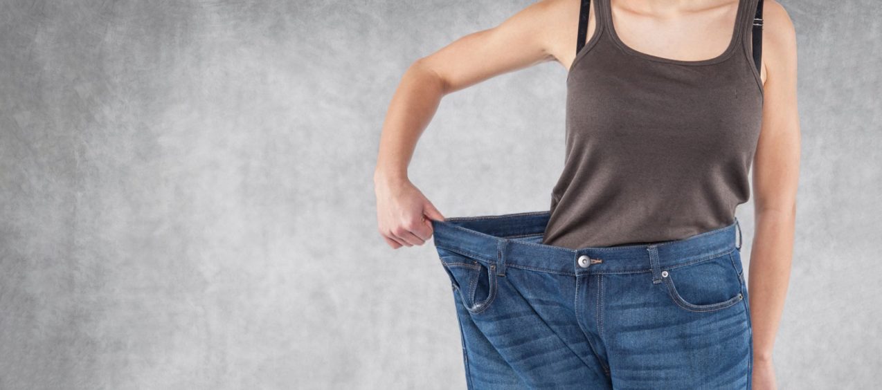 girl shows weight loss by holding side of large pants